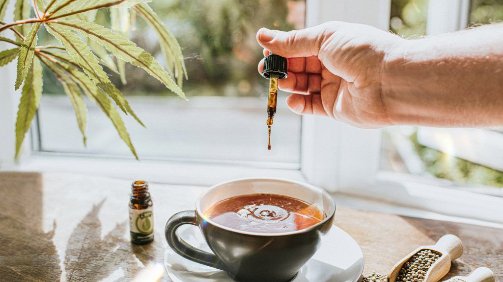 hand adding CBD oil to tea using a dropper