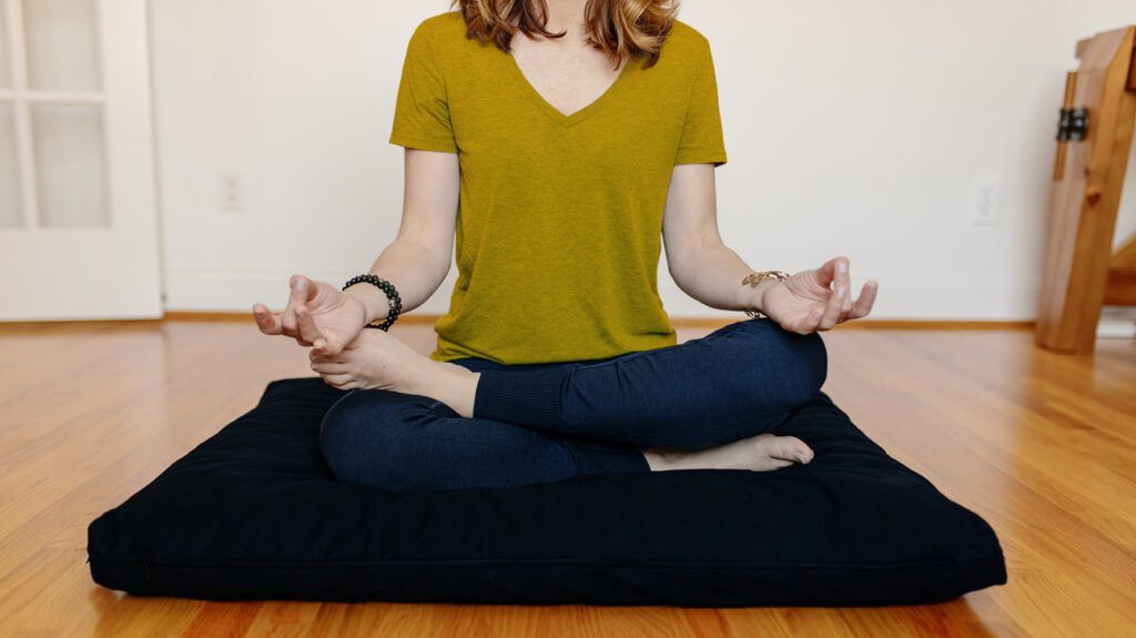 Person sitting on meditation pillow while meditating