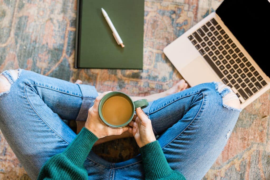 Person sitting on floor with coffee and laptop. Best Ways To Get Paid To Listen To Music. 