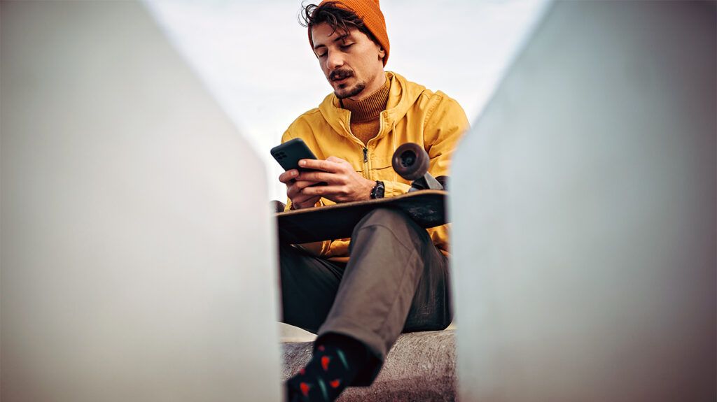 Man sitting with skateboard looking at phone