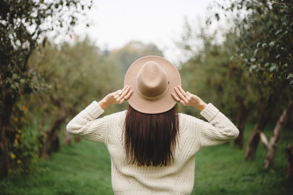 woman walking in field with big brown hat - Pursue mindfulness new year goal